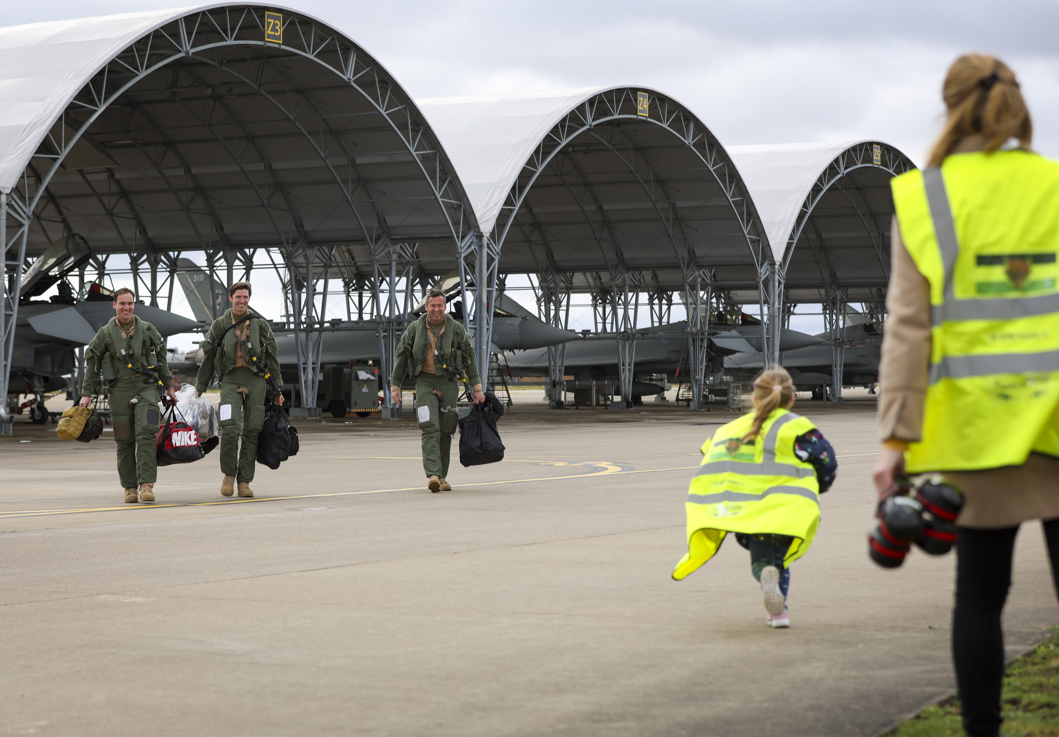 Image shows young girl running towards RAF aviators walking across the airfield, by a Typhoon aircraft.